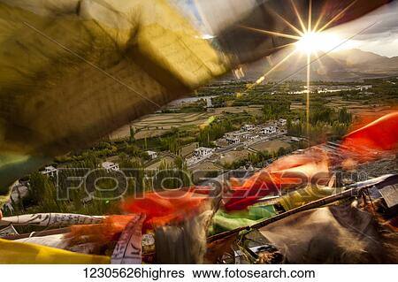 Stock Photograph - The sun sets over a Ladakhi village outside of Leh, viewed through the flapping prayer flags; Ladakh, India. Fotosearch