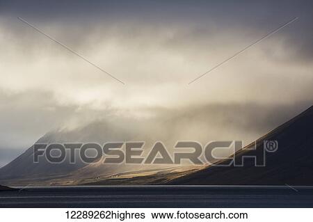 Stock Photograph - The sun shines through storm clouds in the Westfjord region; Iceland. Fotosearch