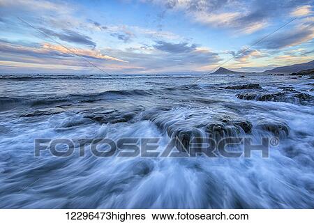 Stock Photograph - The surf of the Atlantic Ocean crash over rocks; West Fjords, Iceland. Fotosearch
