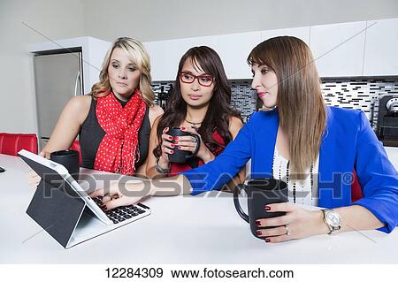Three professional business women looking on social media while taking a break in an office kitchen area; St. Albert, Alberta, Canada View Large Photo Image Stock Photo - Three professional business women looking on social media while taking a break in an office kitchen area; St. Albert, Alberta, Canada. Fotosearch
