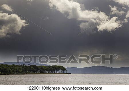 Stock Photograph - Trees and mountains along the coastline under storm clouds; Otter Ferry, Scotland. Fotosearch