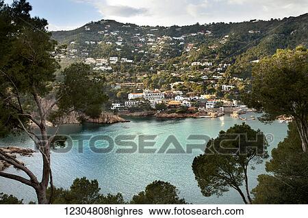 Stock Photograph - Turquoise water in a lake with houses on a hillside; Gerone, Catalonia, Costa Brava, Spain. Fotosearch