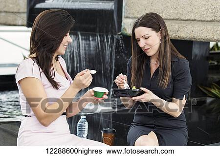 Stock Photograph - Two business women having lunch together in the atrium of an office building; Edmonton, Alberta, Canada. Fotosearch