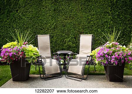Two chairs framed by flowers and a green hedge invite a rest; Surrey, British Columbia, Canada View Large Photo Image Stock Photo - Two chairs framed by flowers and a green hedge invite a rest; Surrey, British Columbia, Canada. Fotosearch