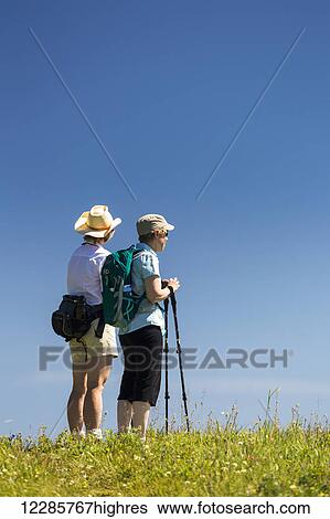 Stock Photograph - Two female hikers on top of a grassy hill with blue sky; Kananaskis Country, Alberta, Canada. Fotosearch