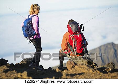 Stock Photograph - Two hikers relaxing enjoying the amazing view from the mountain top.. Fotosearch