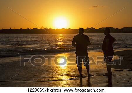 Two men stand in the tide water on a beach at sunset; Caloundra, Queensland, Australia View Large Photo Image Stock Photograph - Two men stand in the tide water on a beach at sunset; Caloundra, Queensland, Australia. Fotosearch