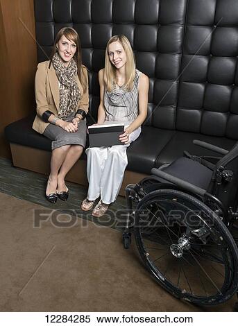 Stock Photography - Two professional business women during a training session in a boardroom, one of which is a paraplegic; St. Albert, Alberta, Canada. Fotosearch