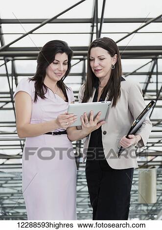 Stock Photograph - Two professional business women using a touch screen in the atrium of an office building; Edmonton, Alberta, Canada. Fotosearch