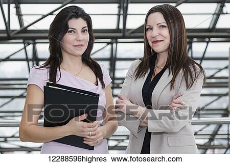 Stock Photograph - Two professional business women using a touch screen in the atrium of an office building; Edmonton, Alberta, Canada. Fotosearch