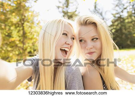 Stock Photograph - Two sisters having fun in a city park in autumn and talking a selfie; Edmonton, Alberta, Canada. Fotosearch