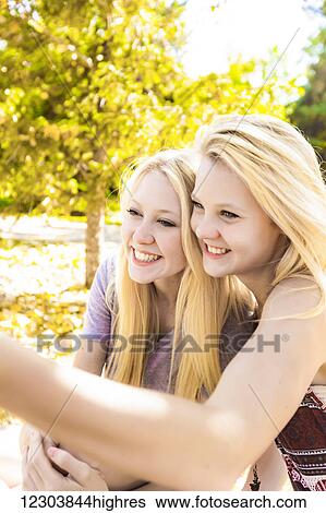 Stock Photograph - Two sisters having fun in a city park in autumn and talking a selfie; Edmonton, Alberta, Canada. Fotosearch