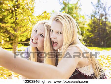 Stock Photograph - Two sisters having fun in a city park in autumn and talking a selfie of themselves and making funny faces; Edmonton, Alberta, Canada. Fotosearch