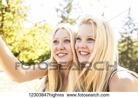 Stock Photograph - Two sisters having fun in a city park in autumn and talking a selfie of themselves; Edmonton, Alberta, Canada. Fotosearch