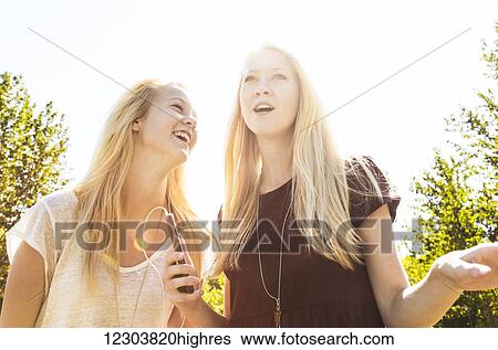 Stock Photograph - Two sisters having fun outdoors and singing together in a city park while listening to music on an MP-3 player; Edmonton, Alberta, Canada. Fotosearch