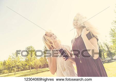 Two sisters having fun outdoors and singing together in a city park while listening to music on an MP-3 player; Edmonton, Alberta, Canada View Large Photo Image Stock Photograph - Two sisters having fun outdoors and singing together in a city park while listening to music on an MP-3 player; Edmonton, Alberta, Canada. Fotosearch
