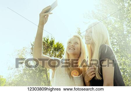 Two sisters having fun outdoors in a city park in autumn and taking selfies of themselves; Edmonton, Alberta, Canada View Large Photo Image Stock Photograph - Two sisters having fun outdoors in a city park in autumn and taking selfies of themselves; Edmonton, Alberta, Canada. Fotosearch