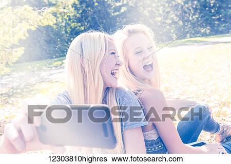 Stock Photograph - Two sisters having fun outdoors in a city park in autumn and laughing at the selfies they have taken of themselves; Edmonton, Alberta, Canada. Fotosearch