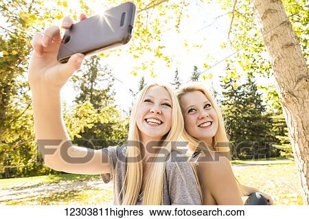 Stock Photograph - Two sisters having fun outdoors in a city park in autumn and taking selfies of themselves; Edmonton, Alberta, Canada. Fotosearch