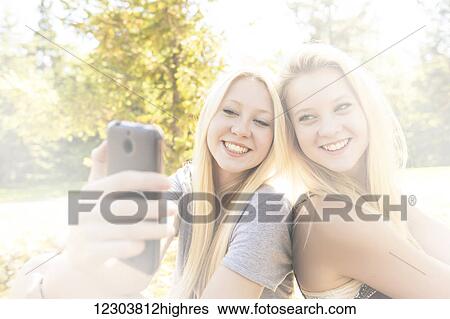 Two sisters having fun outdoors in a city park in autumn and taking selfies of themselves; Edmonton, Alberta, Canada View Large Photo Image Stock Photograph - Two sisters having fun outdoors in a city park in autumn and taking selfies of themselves; Edmonton, Alberta, Canada. Fotosearch