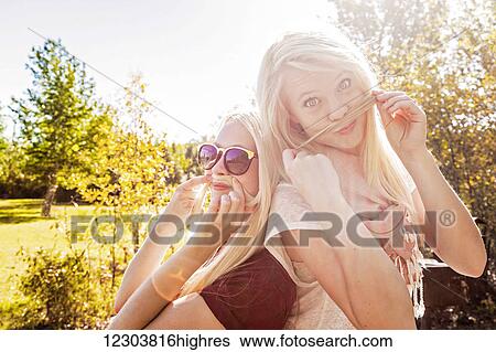 Stock Photograph - Two sisters having fun outdoors in a city park in autumn and posing for the camera while making fake moustaches with their hair; Edmonton, Alberta, Canada. Fotosearch