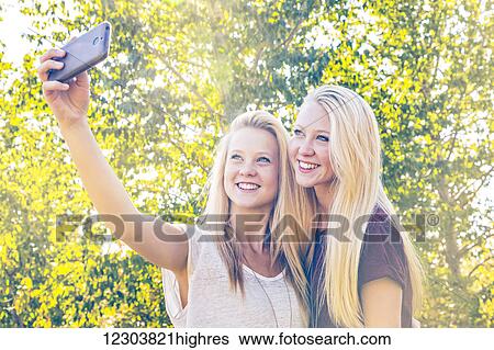 Two sisters having fun outdoors in a city park in autumn and taking selfies of themselves; Edmonton, Alberta, Canada View Large Photo Image Stock Photograph - Two sisters having fun outdoors in a city park in autumn and taking selfies of themselves; Edmonton, Alberta, Canada. Fotosearch