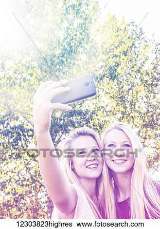 Stock Photograph - Two sisters having fun outdoors in a city park in autumn and taking selfies of themselves; Edmonton, Alberta, Canada. Fotosearch