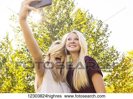 Stock Photograph - Two sisters having fun outdoors in a city park in autumn and taking selfies of themselves when one sister covered the other sister's face with her hair; Edmonton, Alberta, Canada. Fotosearch