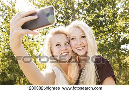 Stock Photograph - Two sisters having fun outdoors in a city park in autumn and taking selfies of themselves; Edmonton, Alberta, Canada. Fotosearch