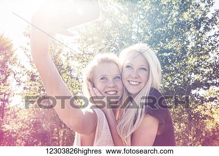 Two sisters having fun outdoors in a city park in autumn and taking selfies of themselves; Edmonton, Alberta, Canada View Large Photo Image Stock Photograph - Two sisters having fun outdoors in a city park in autumn and taking selfies of themselves; Edmonton, Alberta, Canada. Fotosearch
