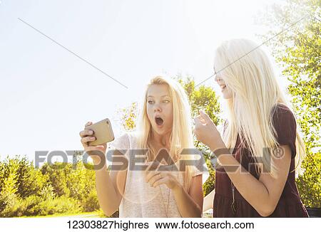 Stock Photograph - Two sisters having fun outdoors in a city park and being shocked at what was posted on social media; Edmonton, Alberta, Canada. Fotosearch