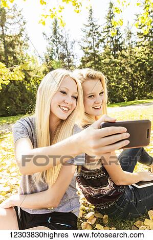 Stock Photograph - Two sisters having fun outdoors in a city park in autumn and taking a selfie; Edmonton, Alberta, Canada. Fotosearch