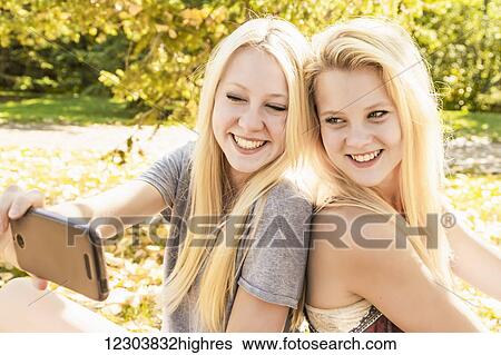 Stock Photograph - Two sisters having fun outdoors in a city park in autumn and taking a selfie; Edmonton, Alberta, Canada. Fotosearch
