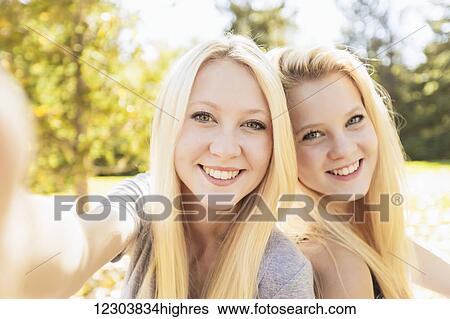 Stock Photograph - Two sisters having fun outdoors in a city park in autumn taking selfie of themselves; Edmonton, Alberta, Canada. Fotosearch