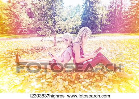 Two sisters having fun outdoors in a city park in autumn looking at social media on their smart phone and tablet; Edmonton, Alberta, Canada View Large Photo Image Stock Photograph - Two sisters having fun outdoors in a city park in autumn looking at social media on their smart phone and tablet; Edmonton, Alberta, Canada. Fotosearch