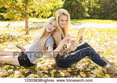 Two sisters having fun outdoors in a city park in autumn looking at social media on their smart phone and tablet; Edmonton, Alberta, Canada View Large Photo Image Stock Photograph - Two sisters having fun outdoors in a city park in autumn looking at social media on their smart phone and tablet; Edmonton, Alberta, Canada. Fotosearch