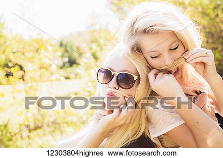 Two sisters having fun together in a city park during autumn and posing for the camera while making fake moustaches with their hair; Edmonton, Alberta, Canada View Large Photo Image Stock Photograph - Two sisters having fun together in a city park during autumn and posing for the camera while making fake moustaches with their hair; Edmonton, Alberta, Canada. Fotosearch
