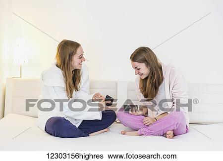 Two teenage sisters wearing pajamas and robes and sitting together on a couch looking at each other's cell phones; Bonn, Nordrhein Westfalen, Germany View Large Photo Image Stock Photograph - Two teenage sisters wearing pajamas and robes and sitting together on a couch looking at each other's cell phones; Bonn, Nordrhein Westfalen, Germany. Fotosearch