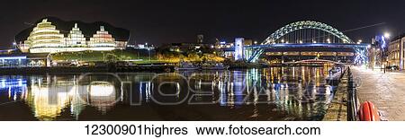 Stock Photograph - Tyne Bridge illuminated at nighttime over River Tyne and illuminated buildings; Newcastle, Tyne and Wear, England. Fotosearch
