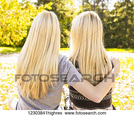 Stock Photograph - View from behind of two sisters hanging out in a city park together in autumn; Edmonton, Alberta, Canada. Fotosearch