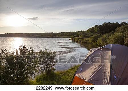 Watching the sunrise from a campsite on Payne Lake, Cardston County; Alberta, Canada. View Large Photo Image Stock Photo - Watching the sunrise from a campsite on Payne Lake, Cardston County; Alberta, Canada.. Fotosearch