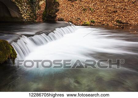 Stock Photograph - Water cascading over a ledge in a river with the riverbank covered with autumn coloured fallen leaves; Naoussa, Greece. Fotosearch