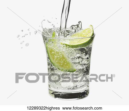Stock Photograph - Water pouring into a glass with lime wedges against a white background; Toronto, Ontario, Canada. Fotosearch