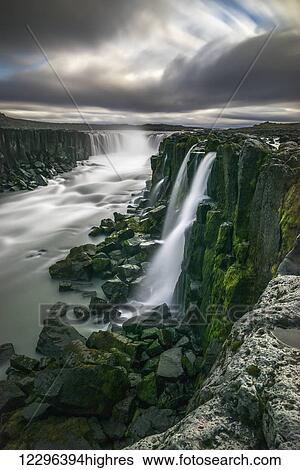 Stock Photograph - Waterfall flowing over moss covered cliffs; Selfoss, Iceland. Fotosearch