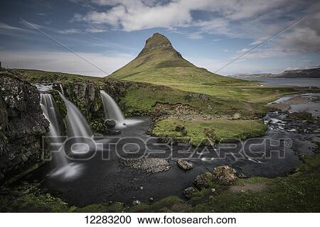 Stock Image - Waterfalls and a rugged green mountain peak on an Icelandic landscape; Iceland. Fotosearch