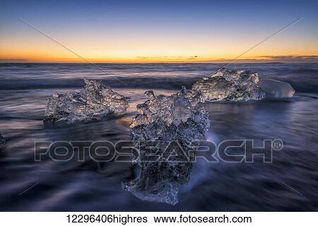 Stock Photograph - Waves break around icebergs on the southern shore of Iceland, near the glacial lagoon of Jokursarlon; Iceland. Fotosearch