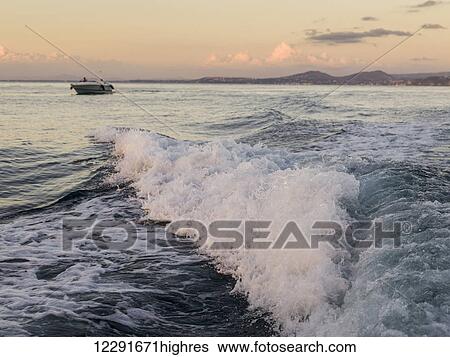 Stock Photograph - Waves rolling into the shore with a boat on the water at sunset; Ischia, Italy. Fotosearch