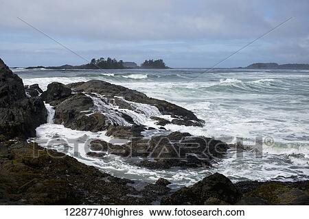 Stock Photograph - Waves washing over rocks and waves along the coastline under a cloudy sky; Tofino, British Columbia, Canada. Fotosearch
