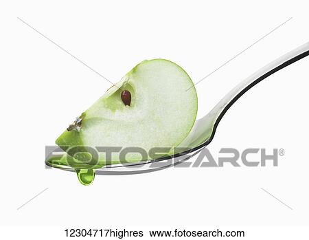 Stock Photograph - Wedge of a green apple in a spoon against a white background; Toronto, Ontario, Canada. Fotosearch