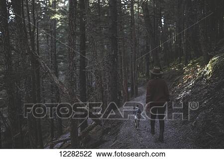 Stock Image - Woman hiking with her dog on a path in the forest, Girdwood, Southcentral Alaska. Fotosearch